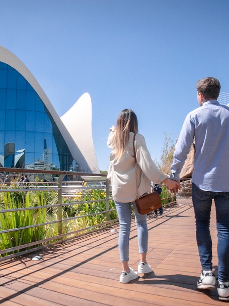 Couple walking towards Oceanogràfic Valencia, Spain, with modern architecture in view.
