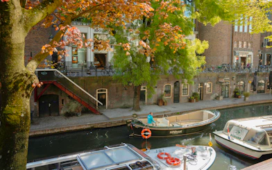 Open boat cruising along Utrecht canal with autumn trees and historic buildings.