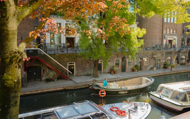Open boat cruising along Utrecht canal with autumn trees and historic buildings.