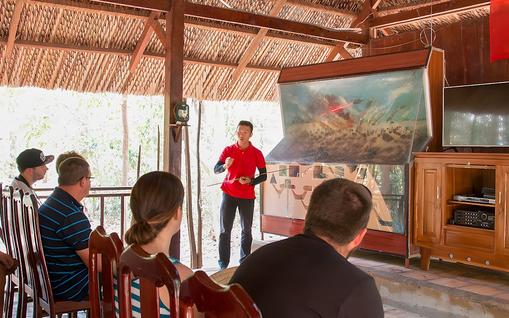 Guide explaining Vietnam war strategies at Cu Chi Tunnels to tourists.