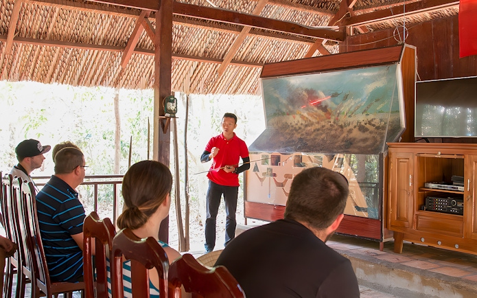 Guide explaining Vietnam war strategies at Cu Chi Tunnels to tourists.