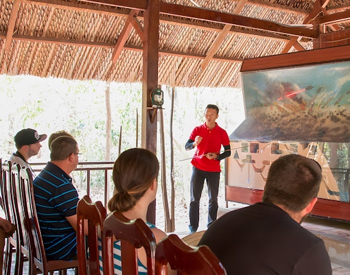 Guide explaining Vietnam war strategies at Cu Chi Tunnels to tourists.