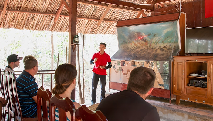 Guide explaining Vietnam war strategies at Cu Chi Tunnels to tourists.