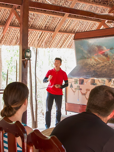Guide explaining Vietnam war strategies at Cu Chi Tunnels to tourists.