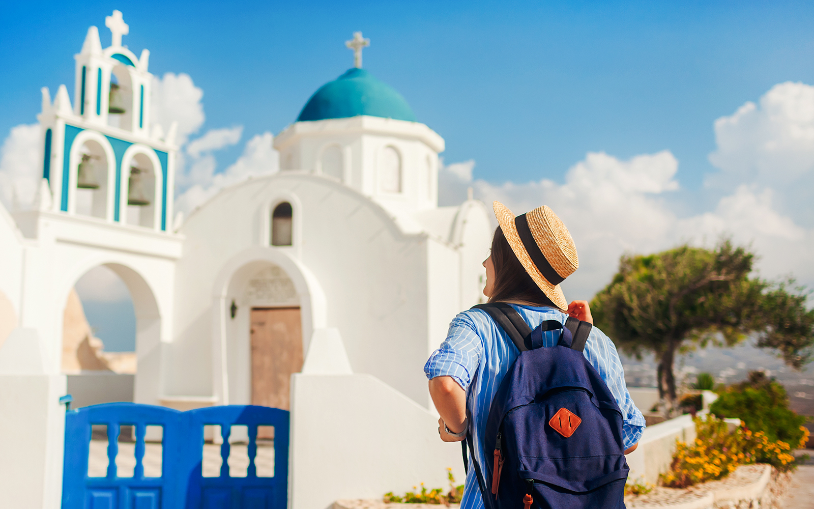 Tourist with backpack walking by a white church with blue dome in Santorini.