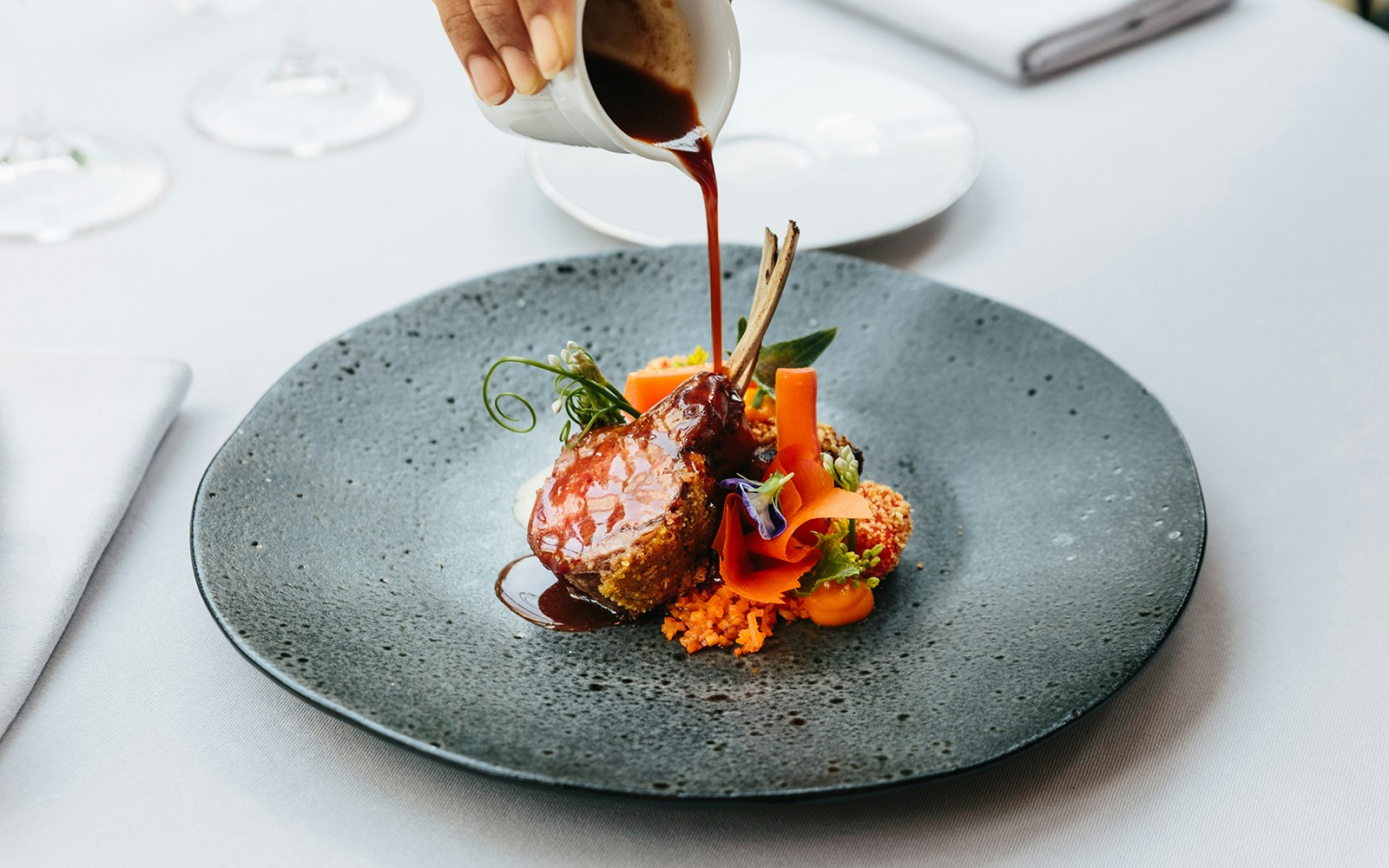 Lamb chops with sauce and vegetables on a fine dining plate.