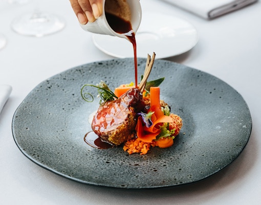 Lamb chops with sauce and vegetables on a fine dining plate.