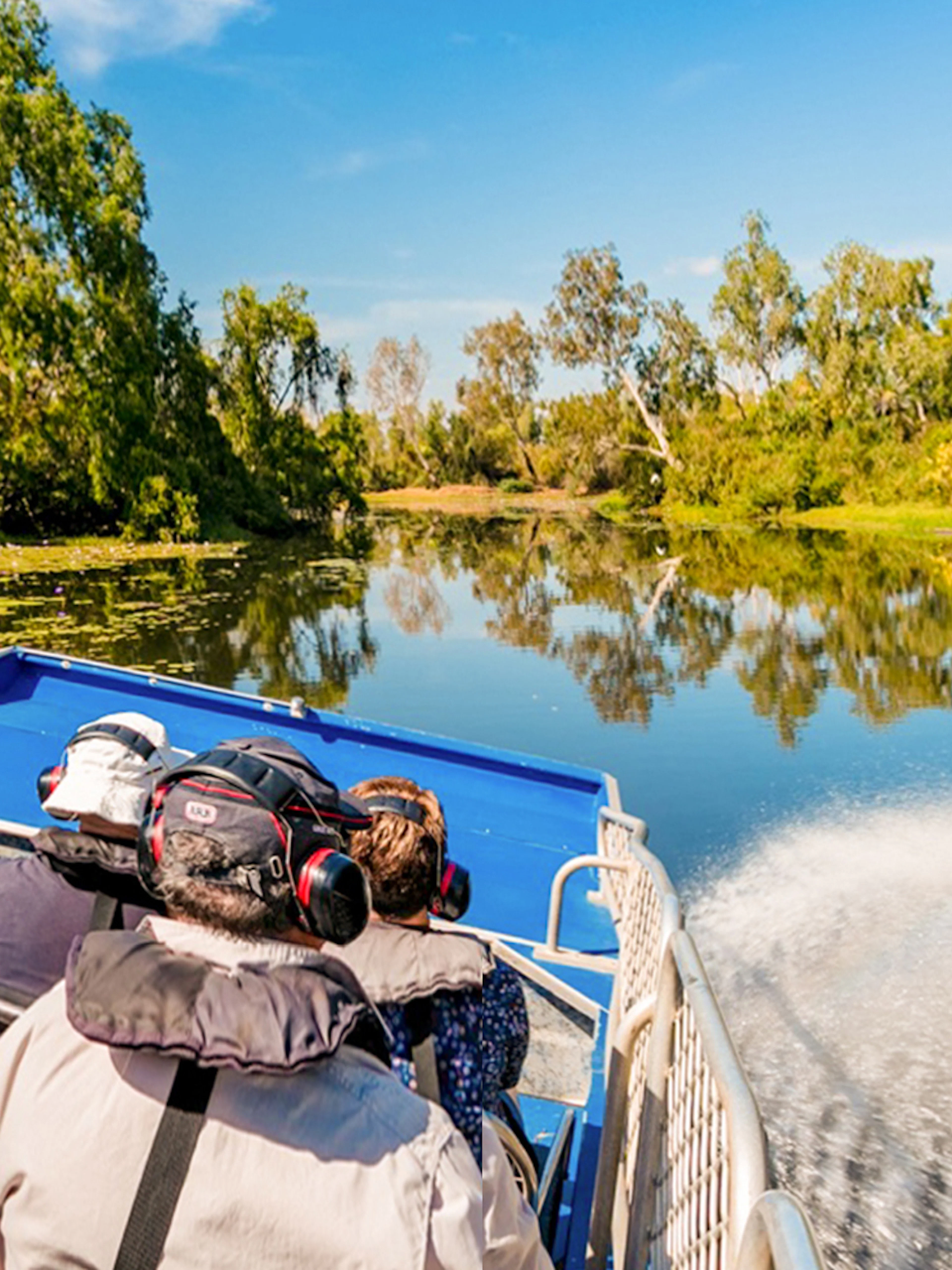 Tourists on a boat tour along the Finniss River, surrounded by lush greenery and clear skies.