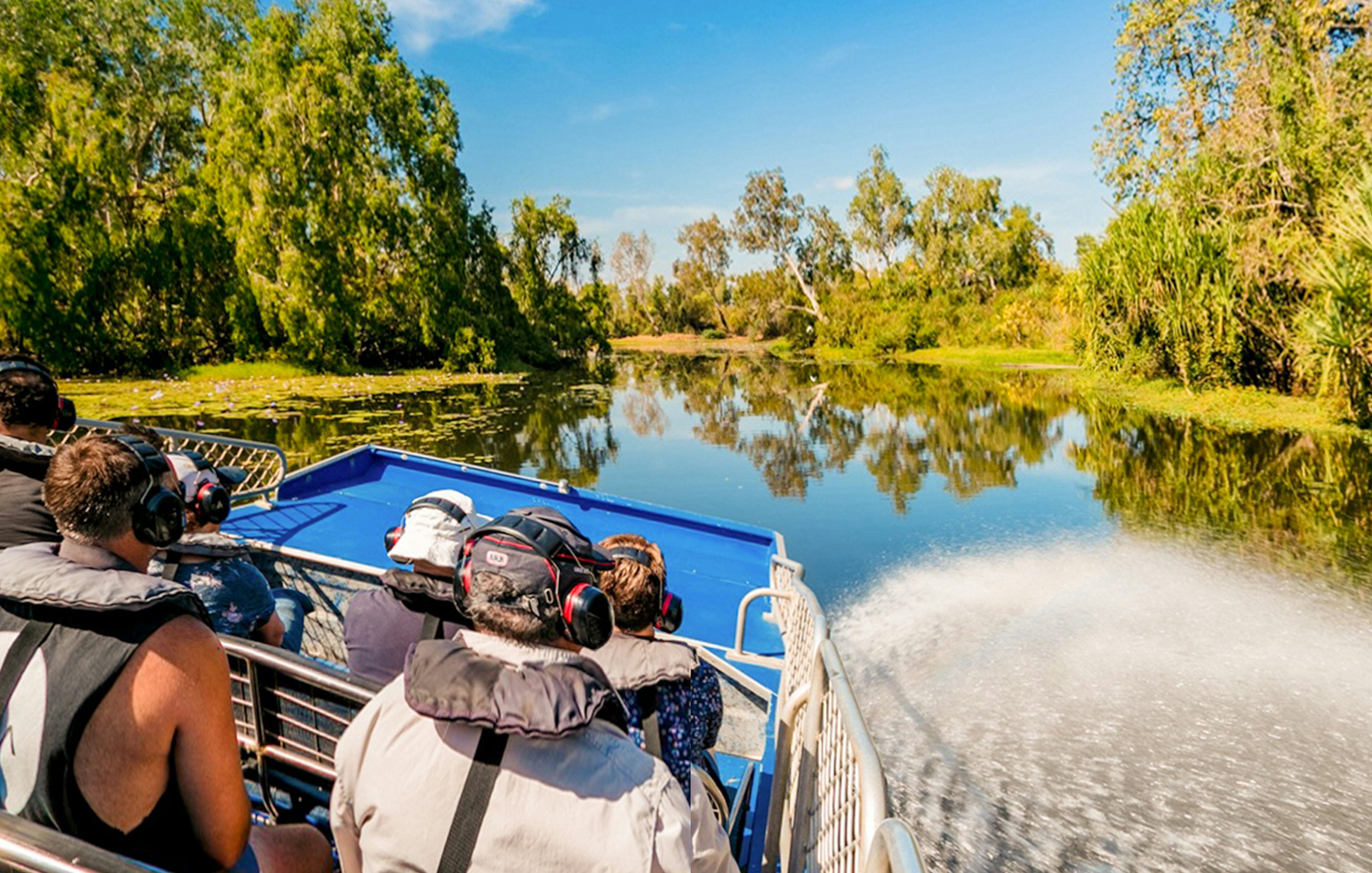 Tourists on a boat tour along the Finniss River, surrounded by lush greenery and clear skies.