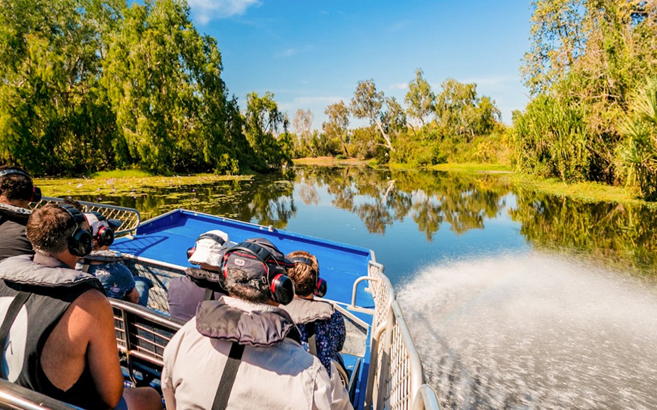 Tourists on a boat tour along the Finniss River, surrounded by lush greenery and clear skies.