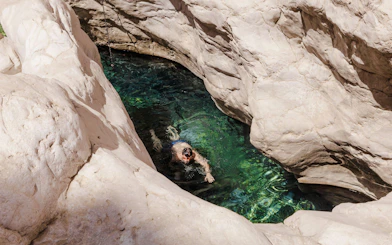 Swimmer in clear water surrounded by rocky cliffs at Wadi Bani Khalid, Oman.