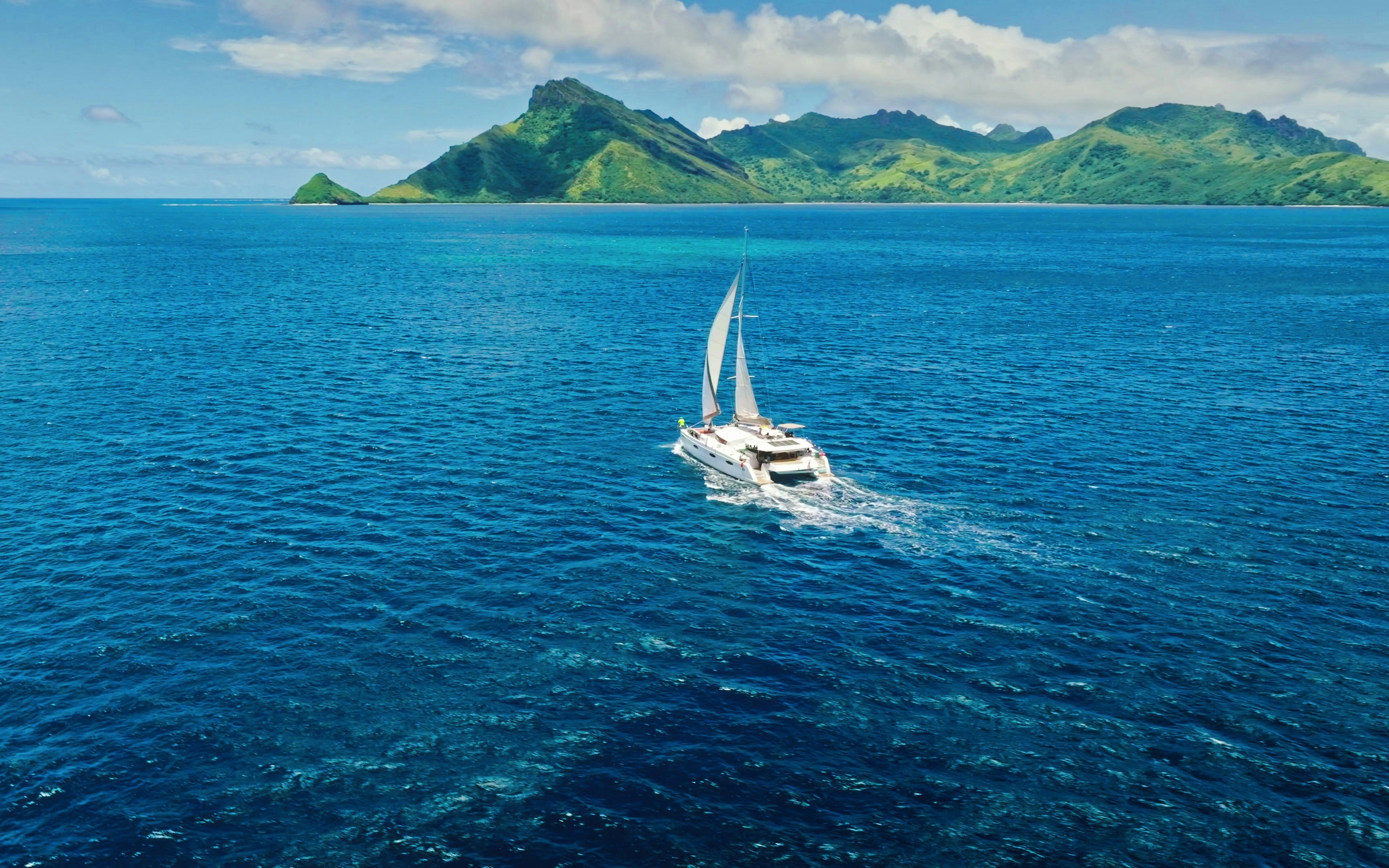 Catamaran sailing near Kuata Island, Fiji, with green mountains in the background.