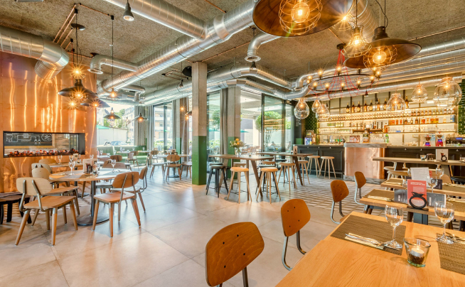Modern restaurant and bar interior with industrial design, featuring wooden tables and a stocked bar.