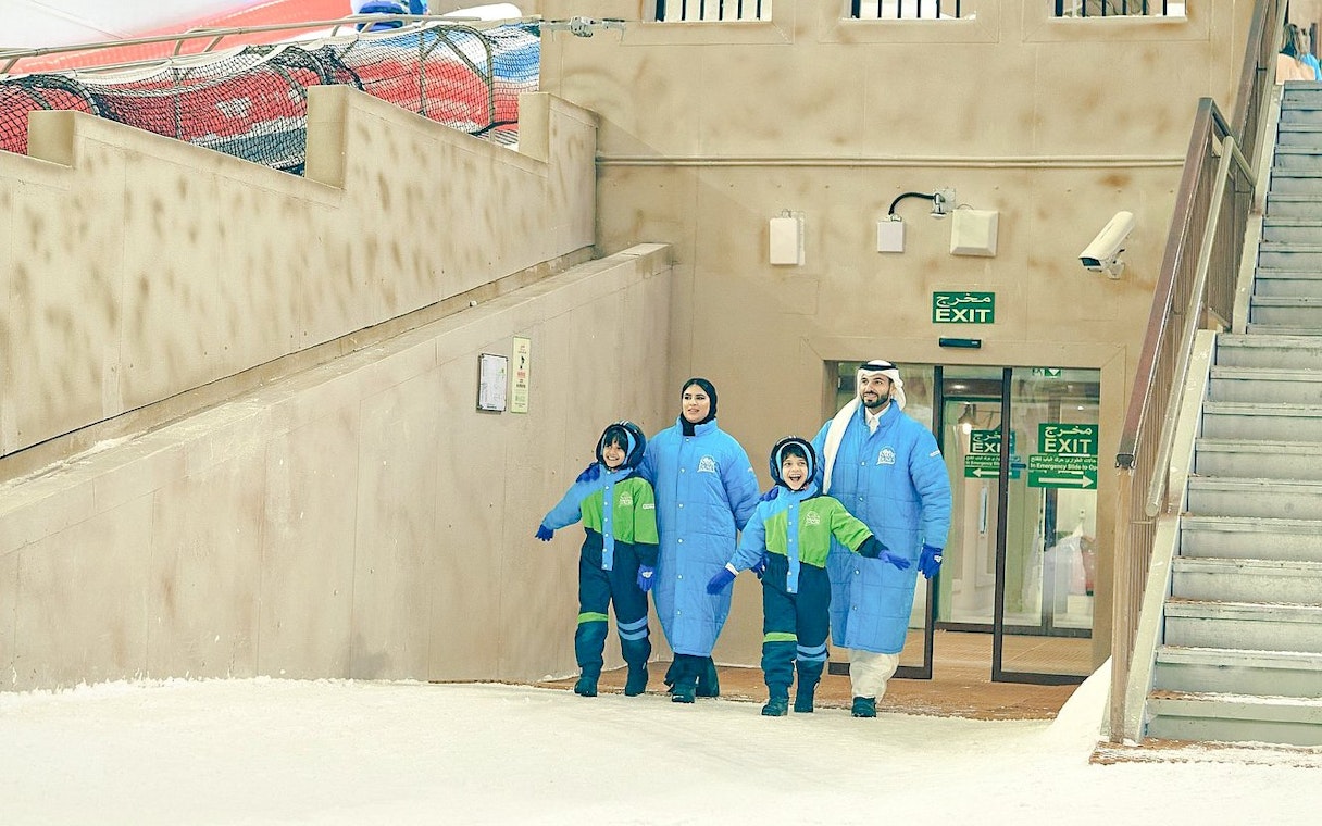 Family in winter gear at Snow Dunes Theme Park entrance.