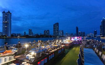 Dinner buffet setup on Alangka Dinner Cruise with Bangkok skyline in the background.