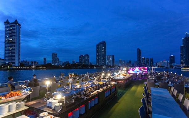 Dinner buffet setup on Alangka Dinner Cruise with Bangkok skyline in the background.
