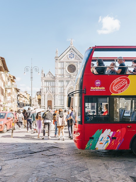 Open-top tour bus near Basilica di Santa Croce in Florence alley.