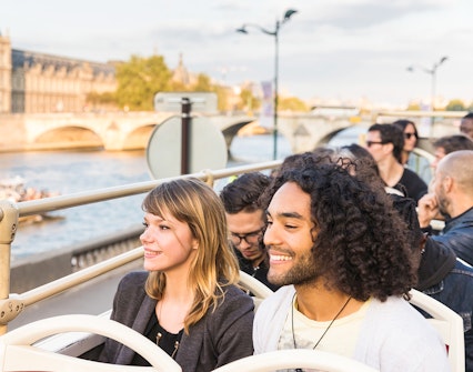 Tourists on Big Bus Paris tour with Eiffel Tower and Seine River in background.
