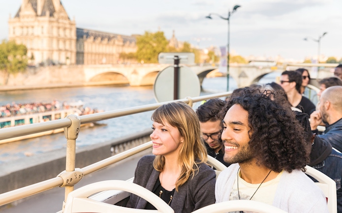 Tourists on Big Bus Paris tour with Eiffel Tower and Seine River in background.