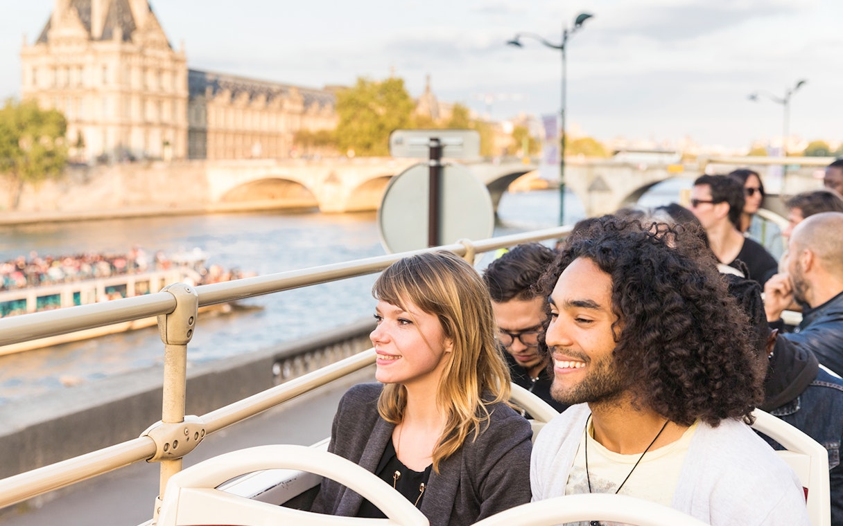 Tourists on Big Bus Paris tour with Eiffel Tower and Seine River in background.