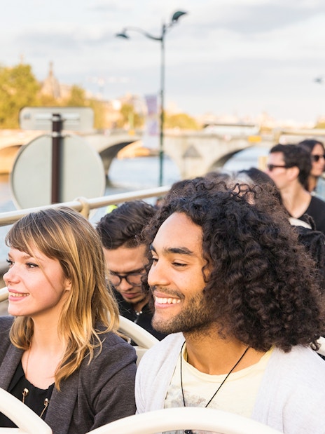Tourists on Big Bus Paris tour with Eiffel Tower and Seine River in background.