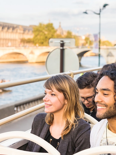 Tourists on Big Bus Paris tour with Eiffel Tower and Seine River in background.
