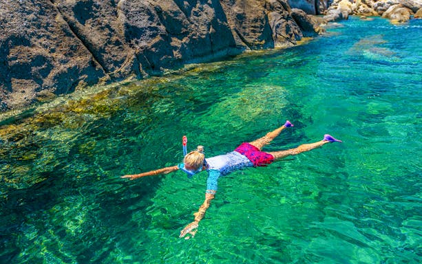 Person snorkeling in clear waters near rocky coast in Cinque Terre, Italy.