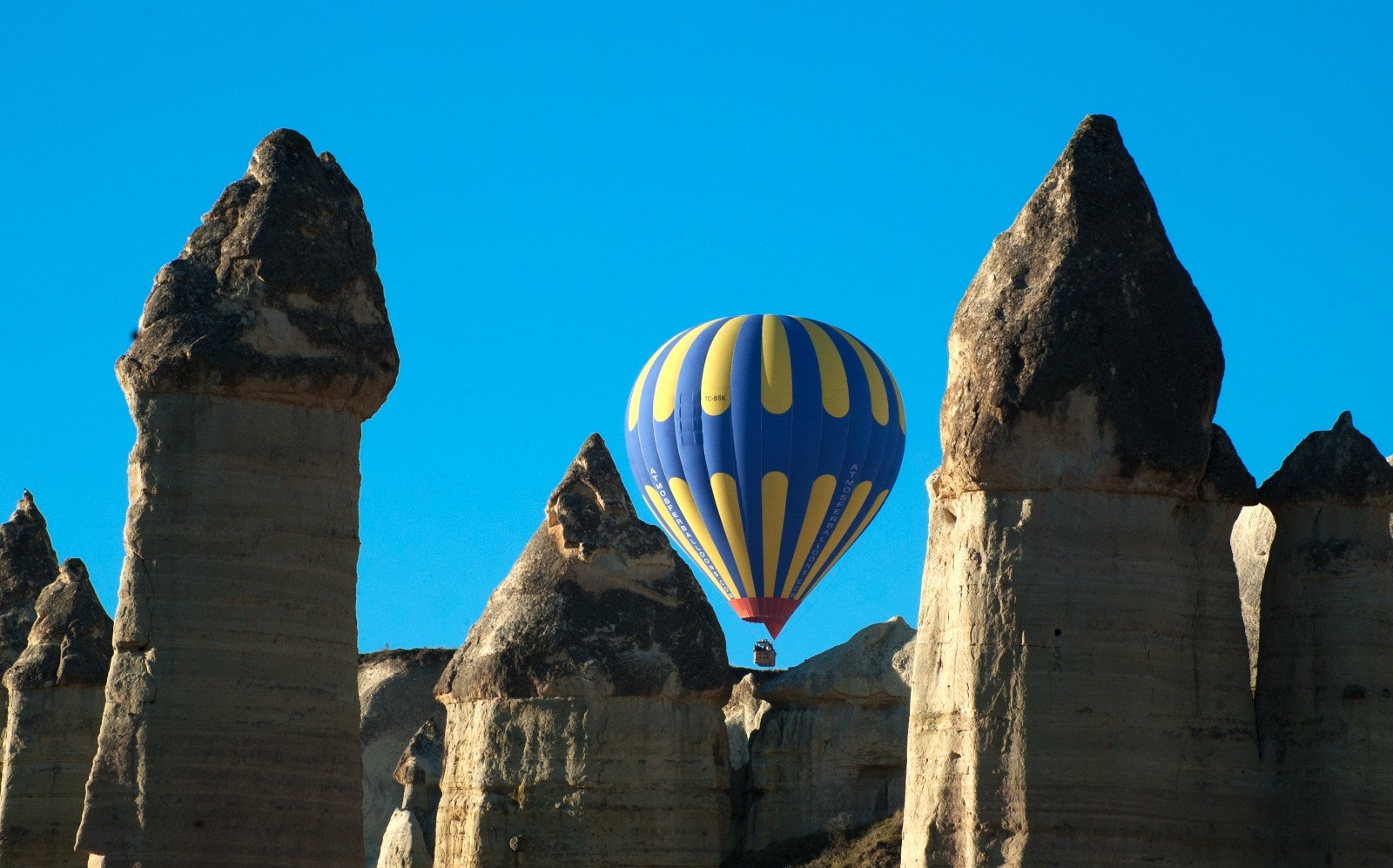 Hot air balloon flying over rock formations in Cappadocia, Turkey.