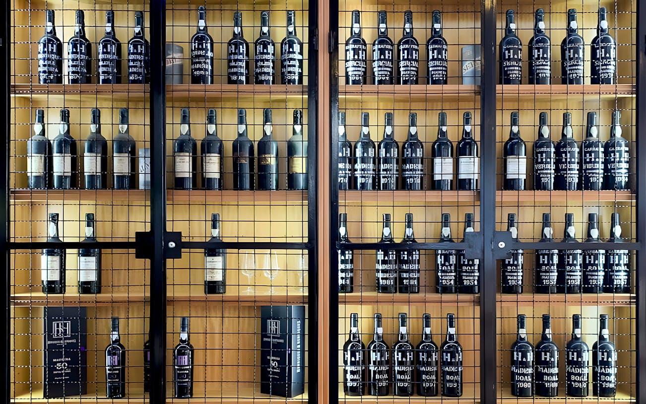 Henriques & Henriques wine bottles displayed on wooden shelves.