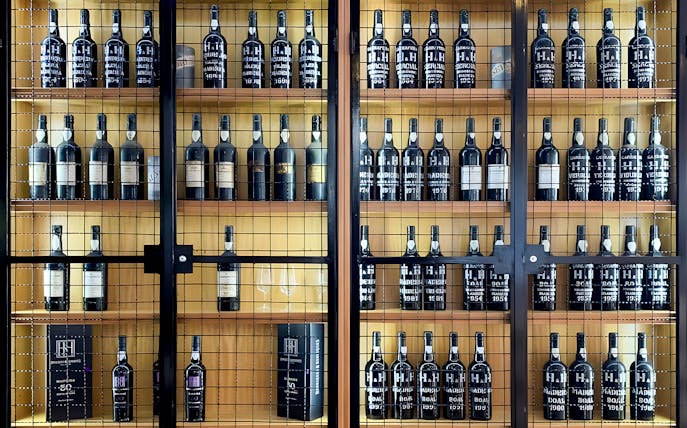 Henriques & Henriques wine bottles displayed on wooden shelves.
