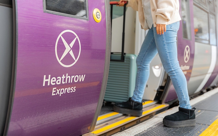 Person boarding Heathrow Express train with luggage at station.