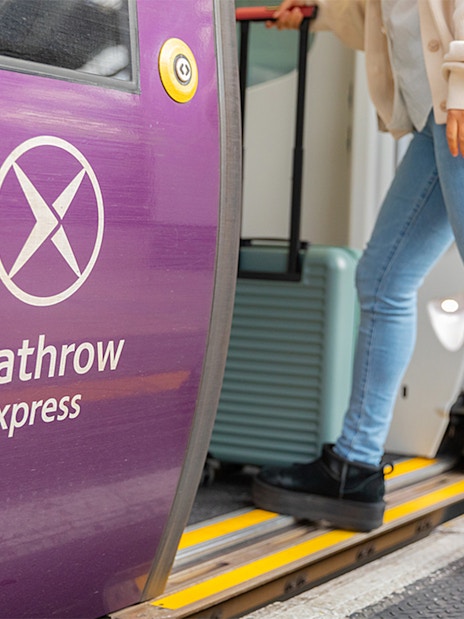 Person boarding Heathrow Express train with luggage at station.