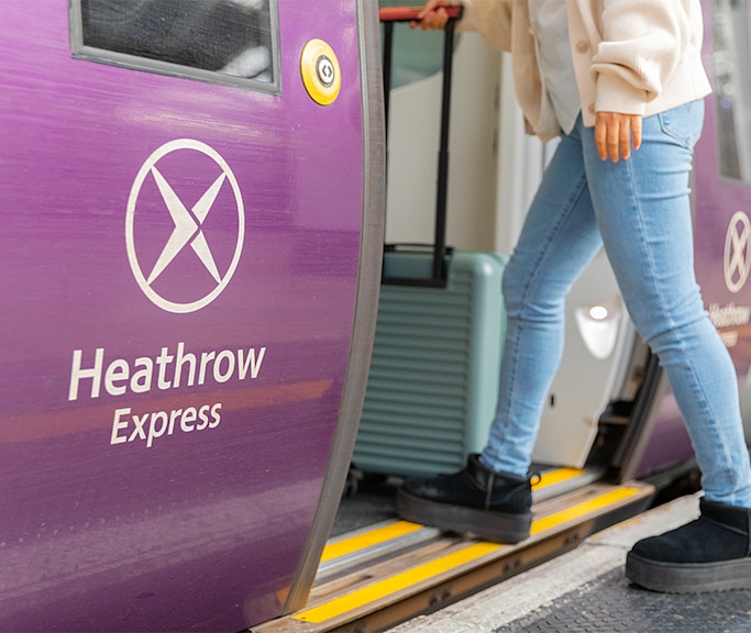 Person boarding Heathrow Express train with luggage at station.