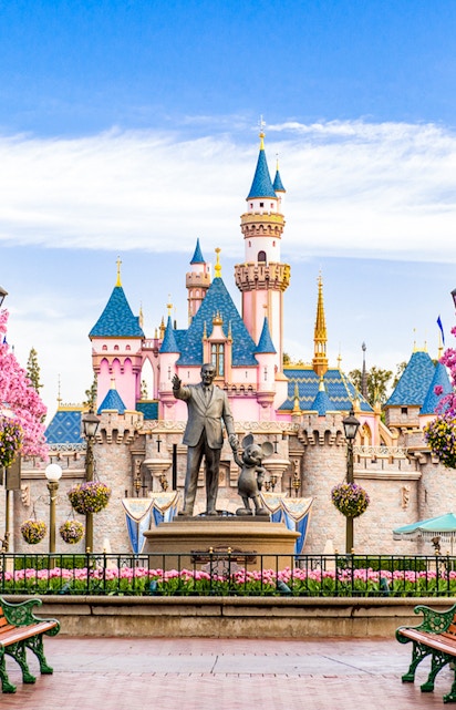 Disneyland California castle with cherry blossoms and blue sky.