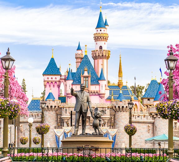 Disneyland California castle with cherry blossoms and blue sky.