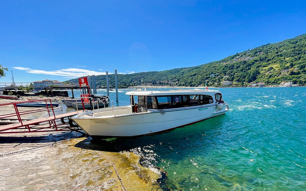 Boat docked at Isole Borromee for Hop-on Hop-off tour, with scenic lake and hills in background.