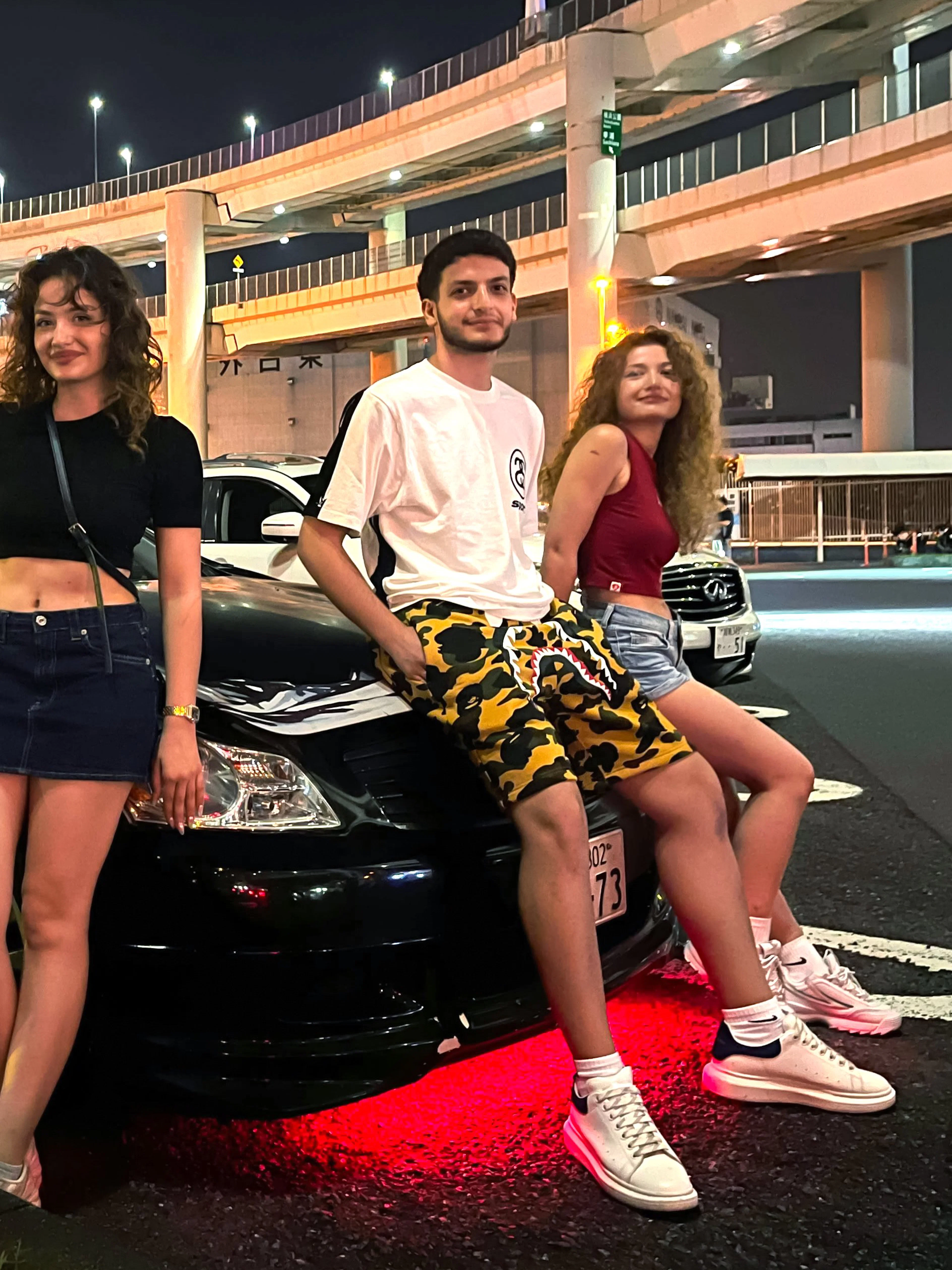 Group posing with custom cars at Daikoku PA during Tokyo Drift JDM Culture Tour.