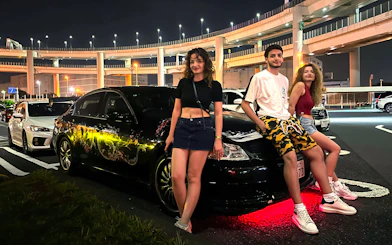 Group posing with custom cars at Daikoku PA during Tokyo Drift JDM Culture Tour.