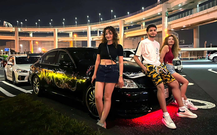 Group posing with custom cars at Daikoku PA during Tokyo Drift JDM Culture Tour.