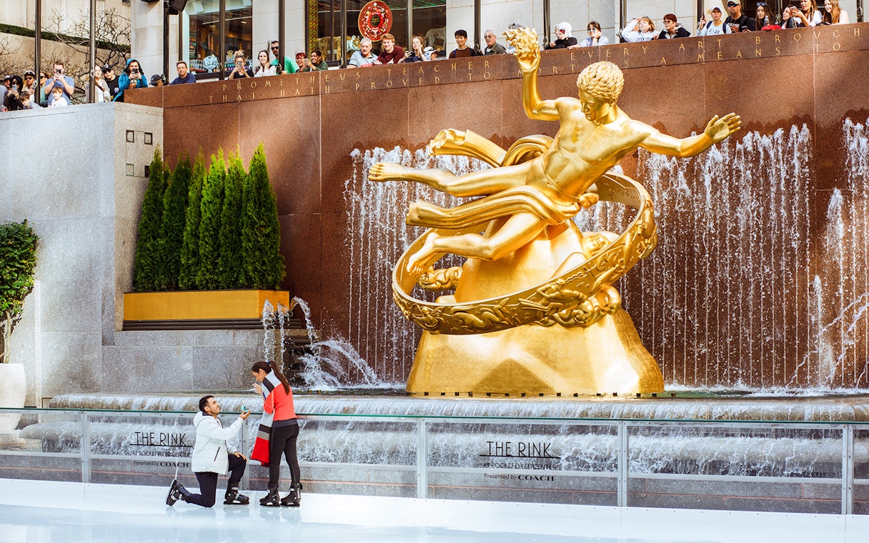 Tourists ice skating at The Rink with Prometheus statue in the background.