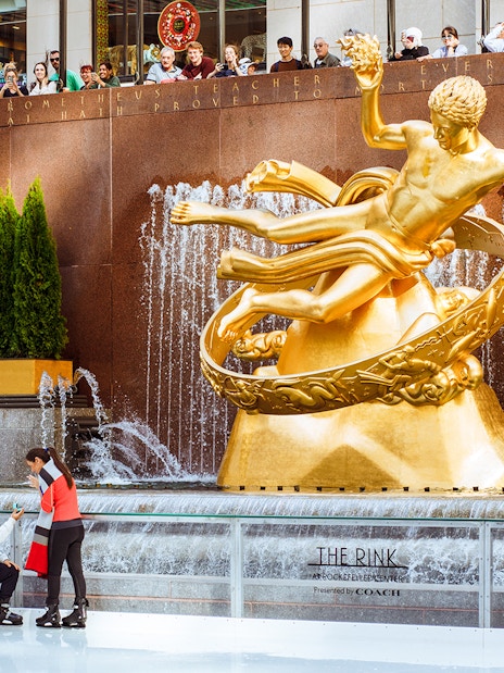 Tourists ice skating at The Rink with Prometheus statue in the background.