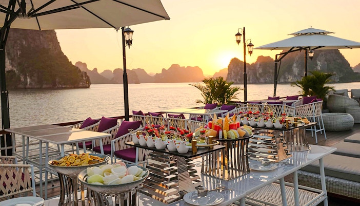 Outdoor dining setup on a 5-Star Irish Cruise in Ha Long Bay at sunset.