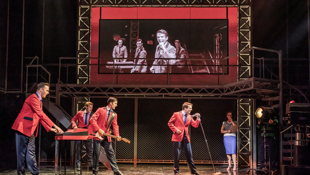 Performers in red jackets on stage during a Jersey Boys musical scene.
