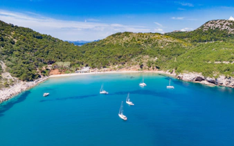 Sailboats anchored in the turquoise waters of Sunj Beach, surrounded by lush green hills.