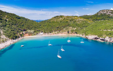 Sailboats anchored in the turquoise waters of Sunj Beach, surrounded by lush green hills.