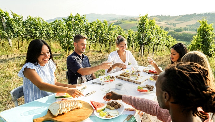 Tourists enjoying lunch at a vineyard in Chianti, Italy, with scenic countryside views.