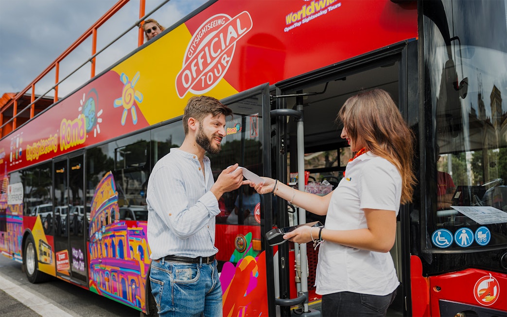 Man receiving ticket for Rome night tour on open-top bus.