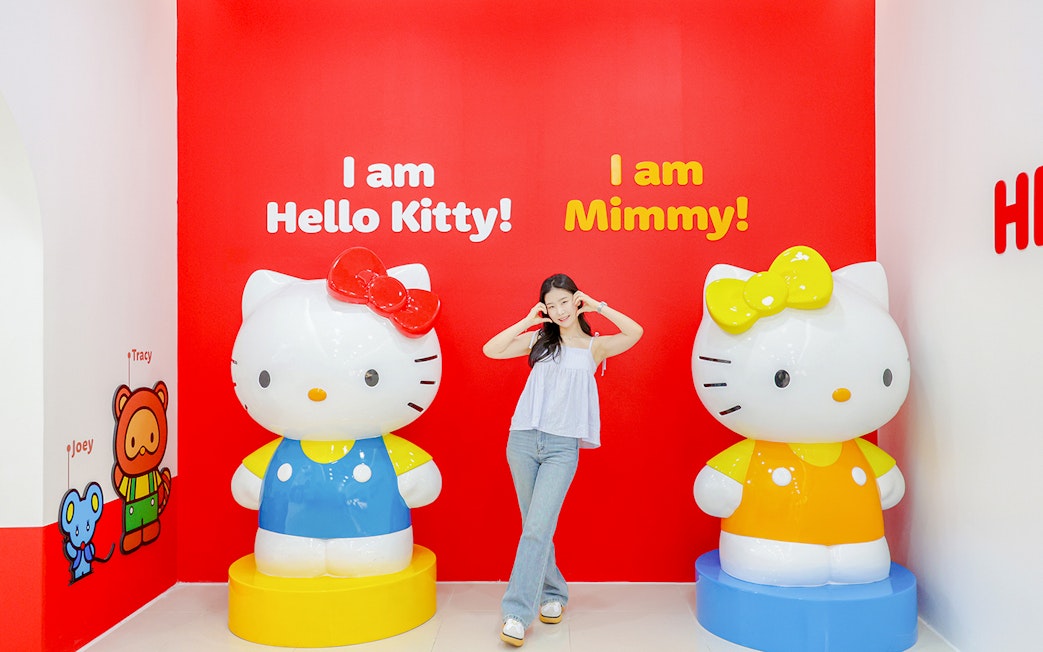 Tourist posing with Hello Kitty and Mimmy statues at Hello Kitty Island.