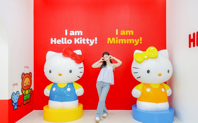 Tourist posing with Hello Kitty and Mimmy statues at Hello Kitty Island.