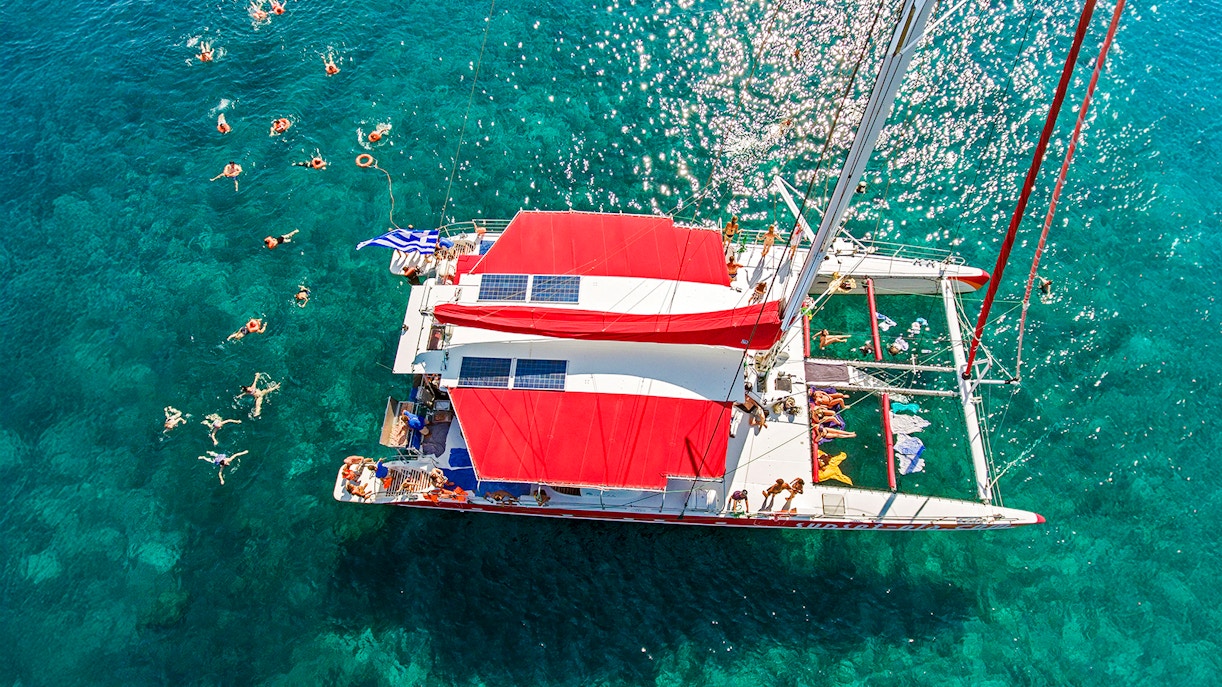 Aerial view of a catamaran cruise with swimmers in Santorini, Greece.